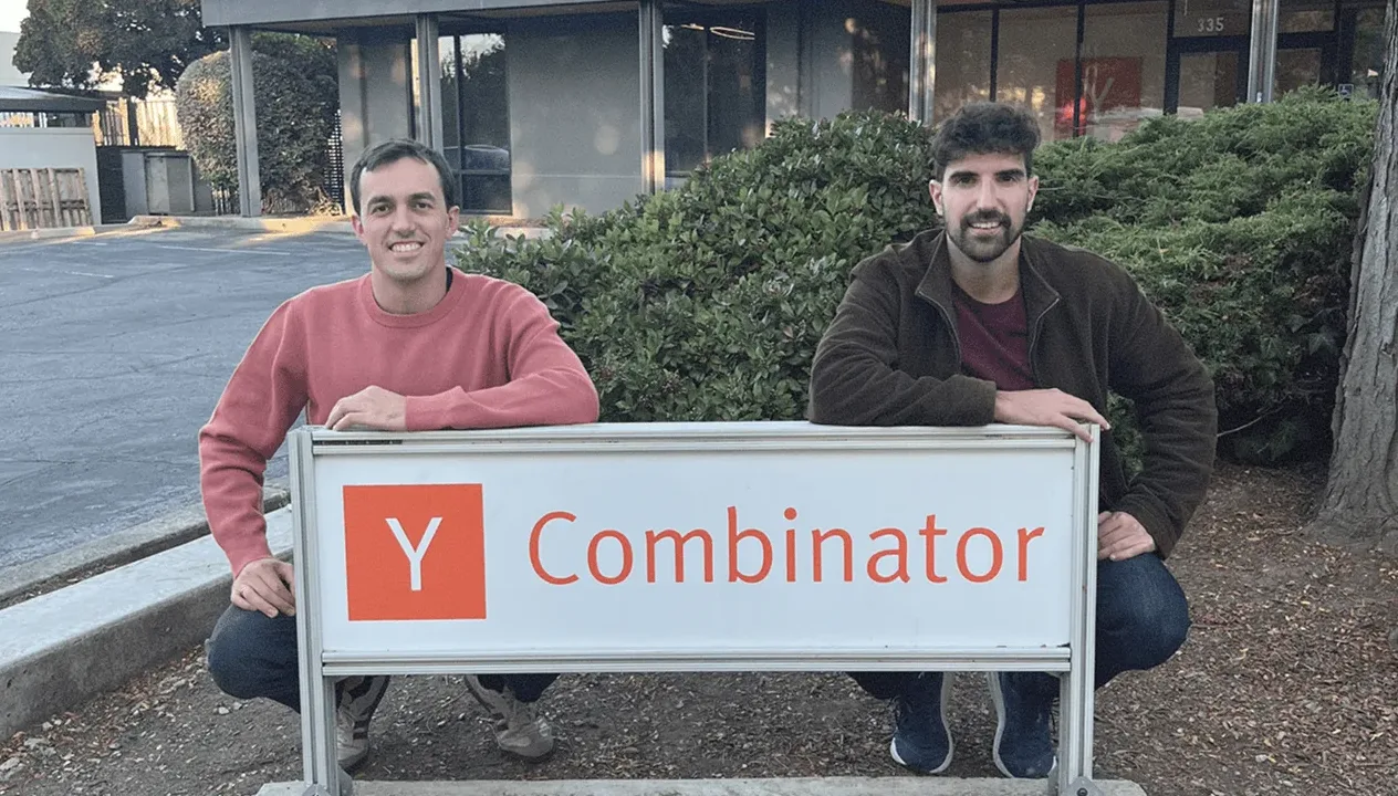 Pablo Omenaca and Toni Lopez, Karumi's founders, crouching behind a Y Combinator sign
